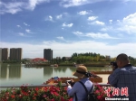 蓝天白云下的新区人工湖风景如画，吸引媒体代表拿起相机记录湖光潋滟的景色。　史静静 摄 - 甘肃新闻