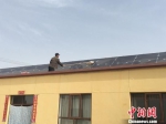 甘肃酒泉市瓜州县广至藏族乡新堡村，村民芦满财在自家的屋顶擦拭光伏电板。　张婧 摄 - 甘肃新闻